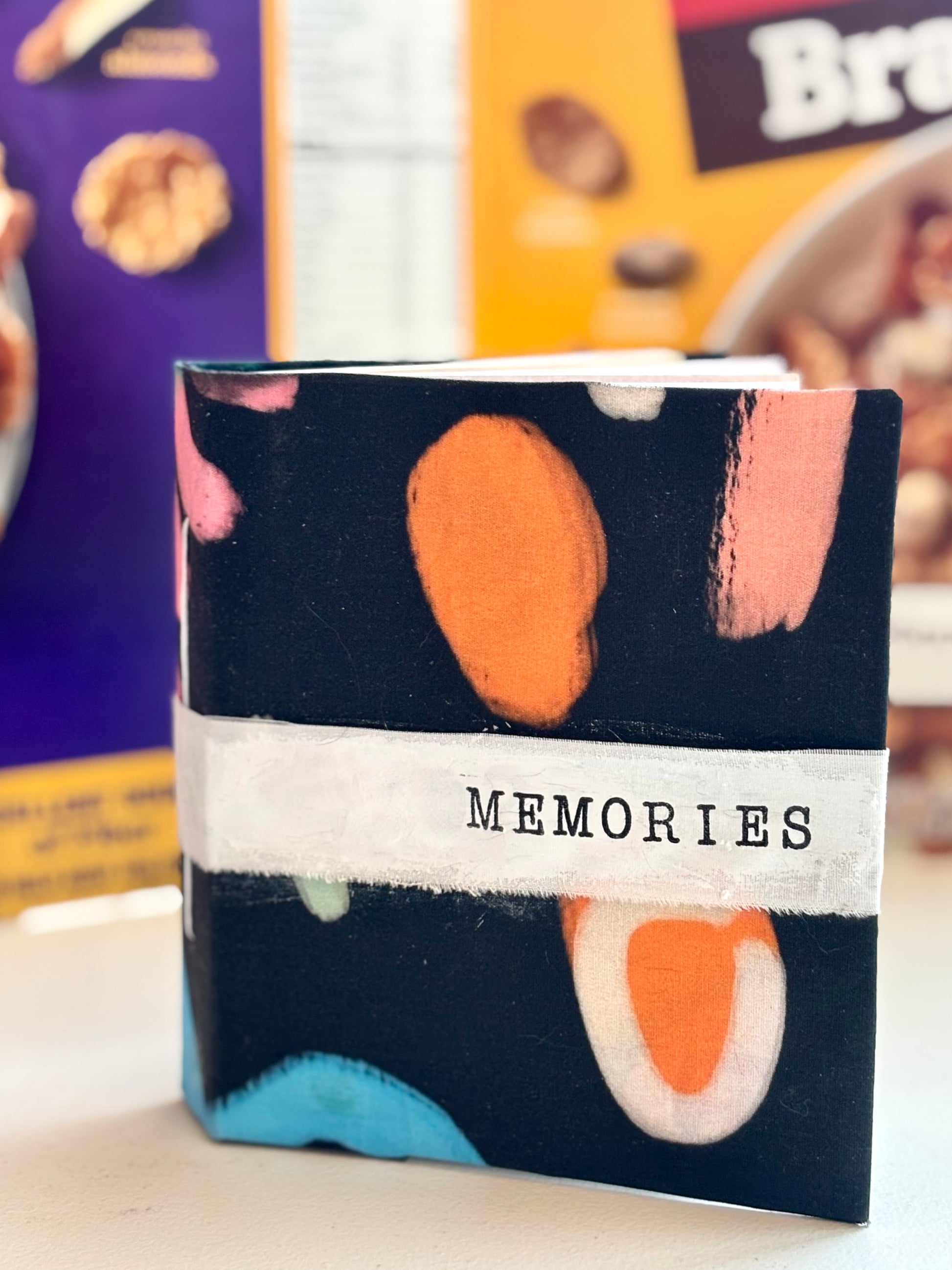 Small notebook with colorful abstract design and 'MEMORIES' text on a blurred background